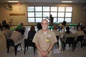 Rob Daughenbagh, a Northpoint Training Center inmate, is photographed by Robby Henson while other participants in the Voices Inside program perform a read through of a play in the background. 